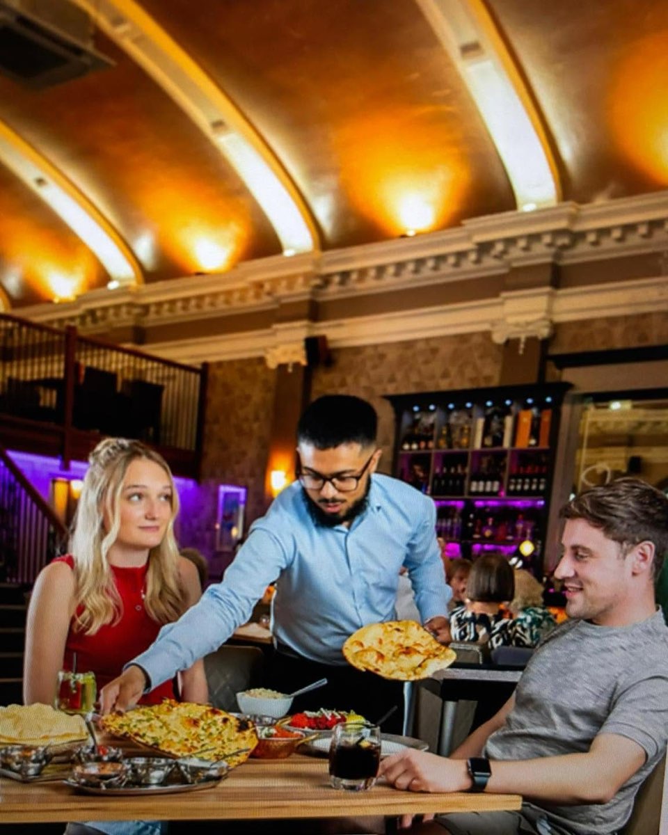 A waiter serving curries to diners under Ba'Bursi's arched, lit ceiling